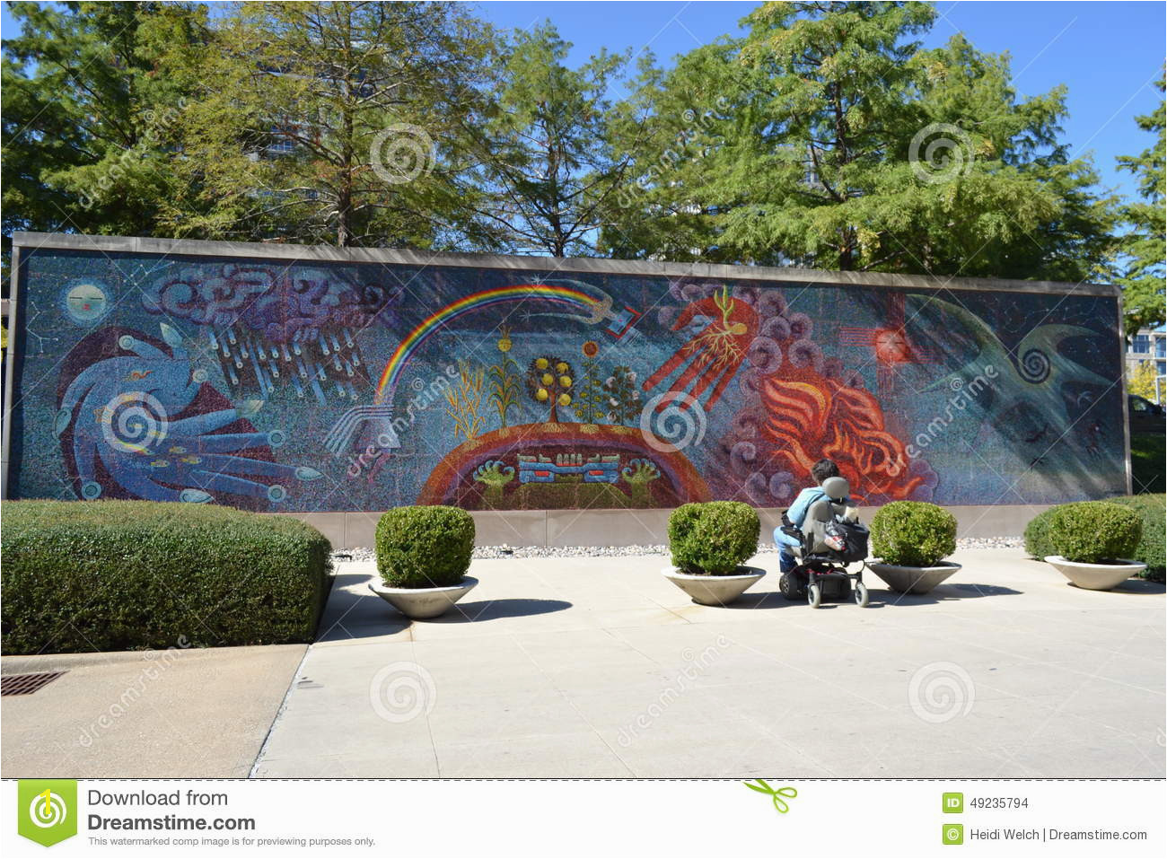Looking at a mural painted on a wall outside the Dallas Museum of Art one person in a wheelchair can be seen studying the mural