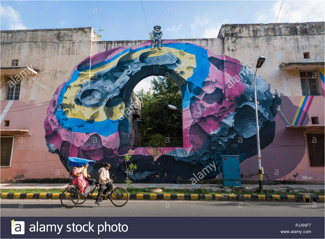 rickshaw rider and passenger ride past wall mural on building painted by swiss artists nevercrew in lodhi colony new delhi india PJXNF7